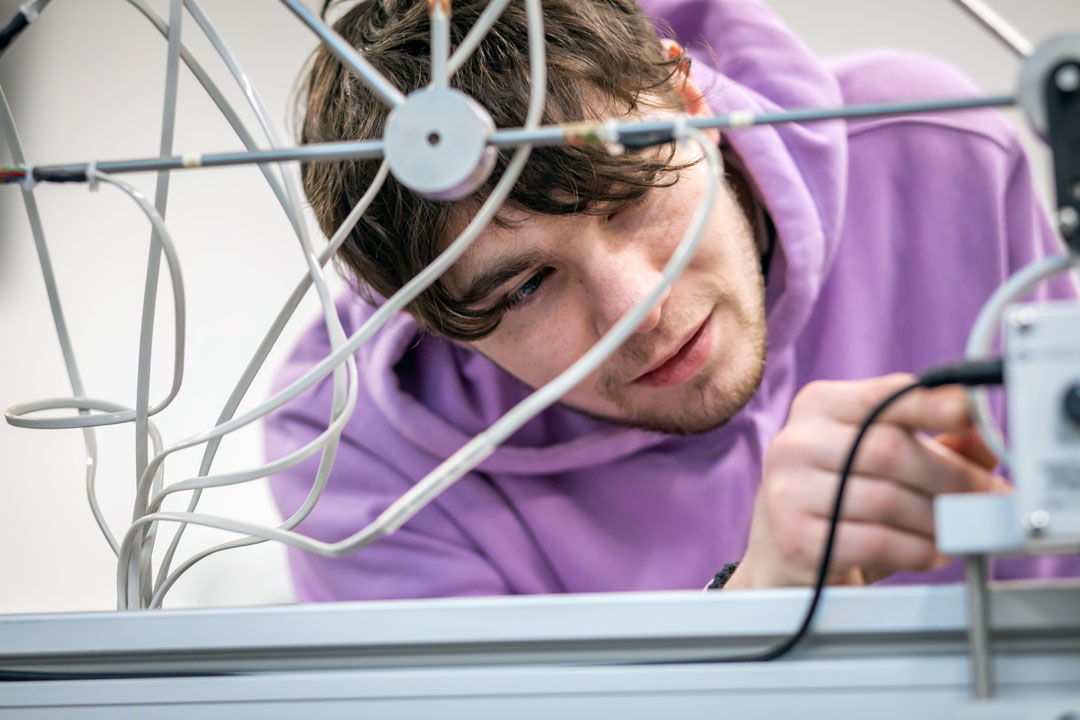A student in a purple hoodie carefully adjusting wires on a mechanical assembly, focused on a hands-on engineering project.
