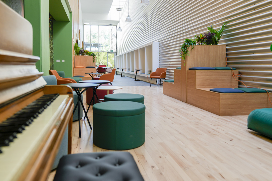 Stylish student lounge with circular stools, lush green sofas, and a mural of tropical plants.