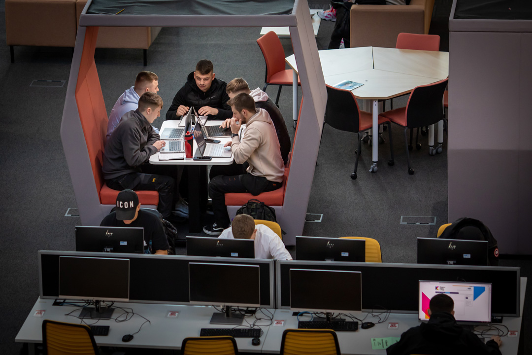 Group of male students working together on laptops in a study pod at Glasgow Kelvin College’s Springburn campus, with others using nearby desktop computers.