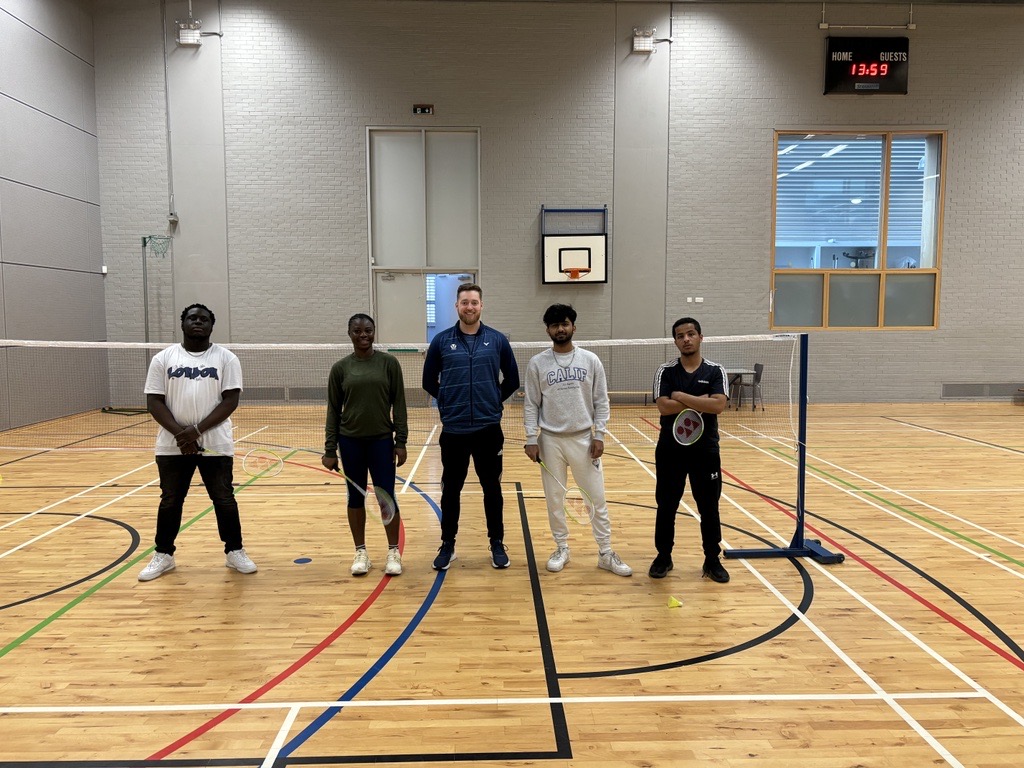 Group of students and a coach posing in the gym hall at Glasgow Kelvin College after a badminton session, standing on either side of the net.