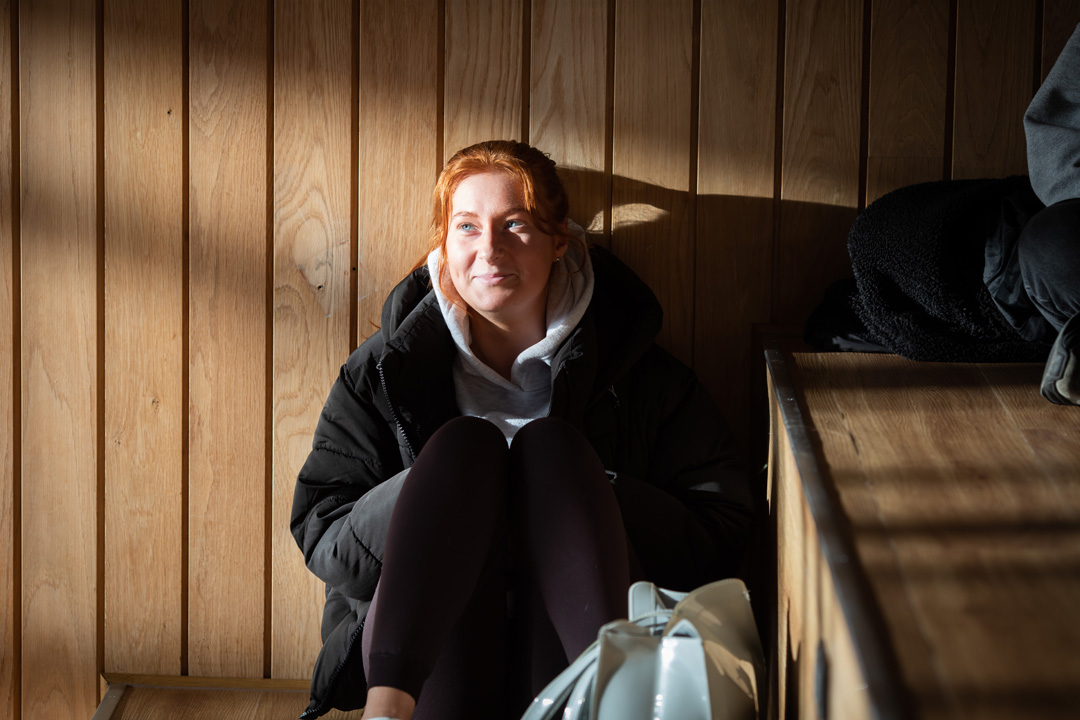 Student sitting in sunlight on wooden steps at Glasgow Kelvin College Springburn campus, wearing casual clothes and smiling softly