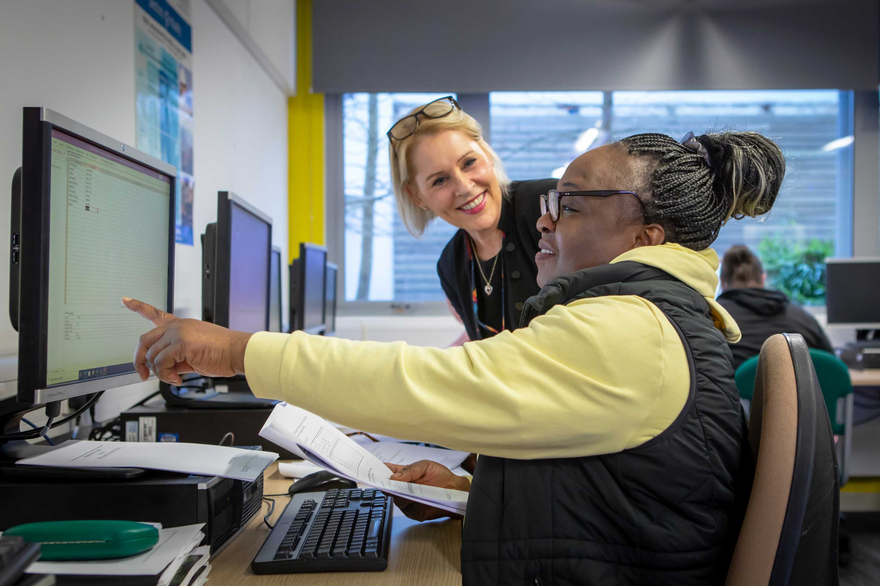 Lecturer assisting a student at a computer, with both looking at the screen as the student points at the content.