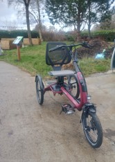 Three-wheeled adapted bike designed for accessible cycling, shown in an outdoor community garden setting.