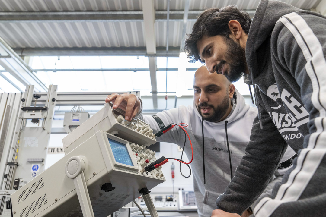 Two students working together on an oscilloscope, adjusting settings to analyze waveforms in an electronics engineering lab.