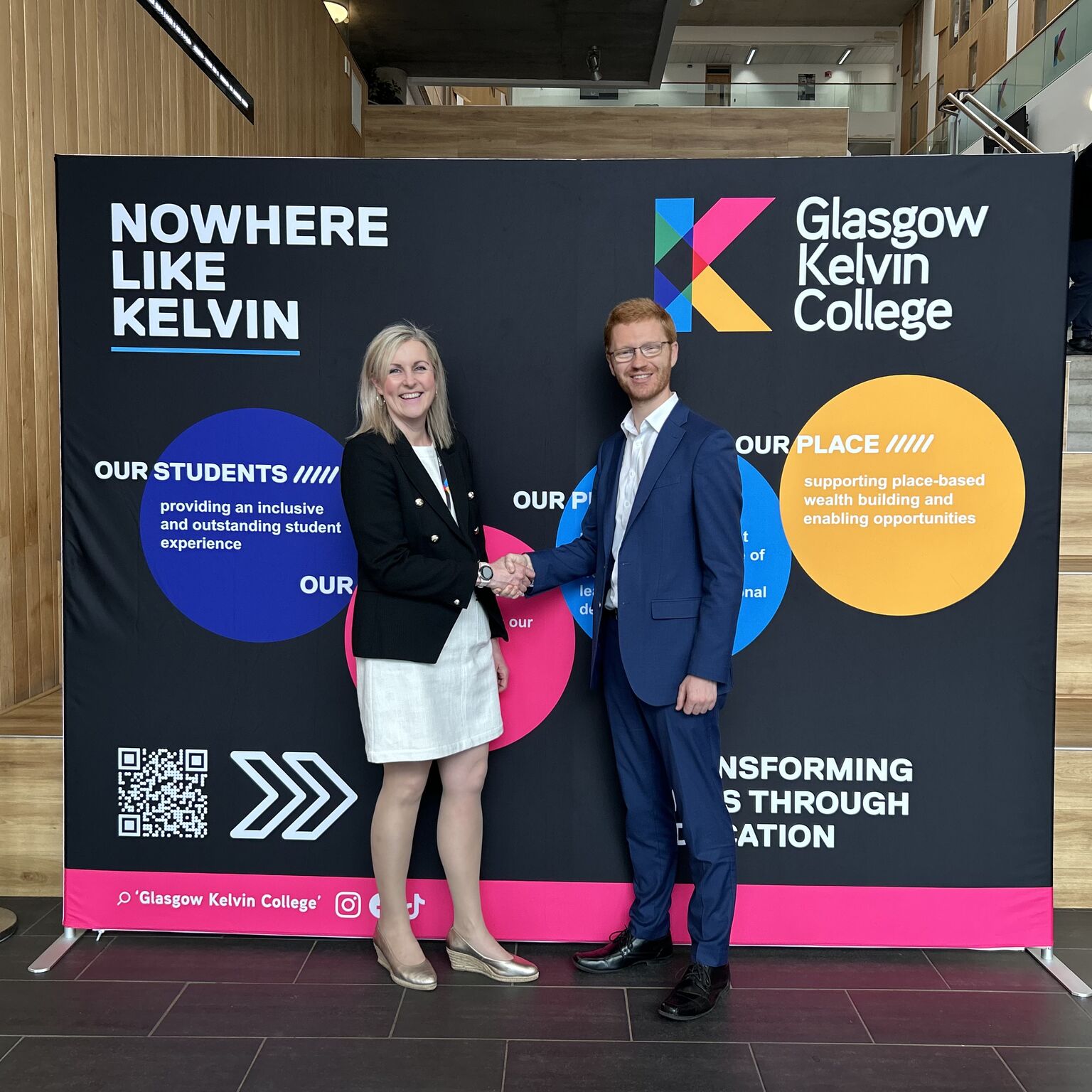 Handshake between Glasgow Kelvin College representative and visiting partner in front of college branding display.