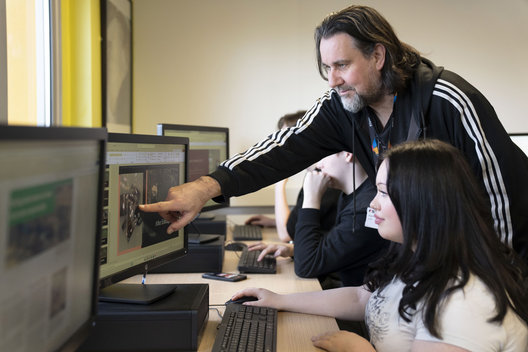 Lecturer pointing to a computer screen while assisting students in a Glasgow Kelvin College digital media classroom.