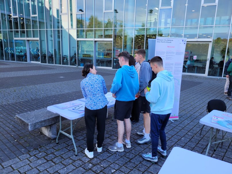 Glasgow Kelvin College students and staff gathered around an information table outside the campus building, exploring new active travel network maps and resources.
