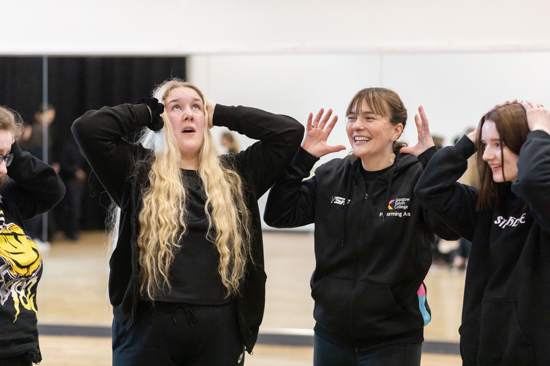 Performing arts lecturer guiding students through a drama activity, with the group responding using physical expression.