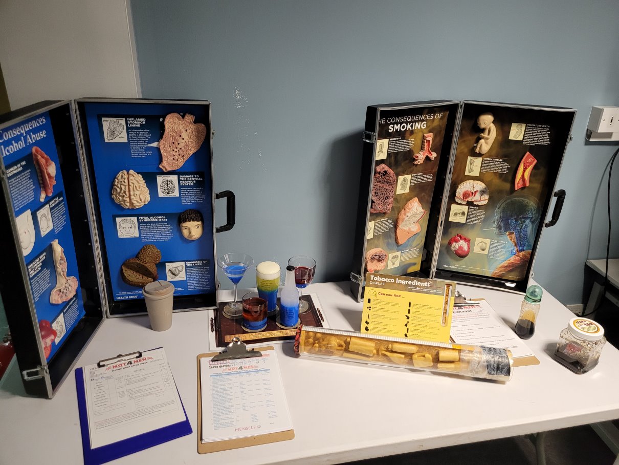 Educational display table at Glasgow Kelvin College showing the health consequences of alcohol abuse and smoking, with anatomical models, charts, and information leaflets.